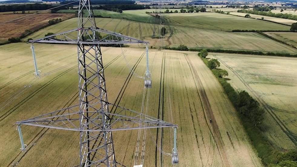 Aerial view of a high-voltage transmission tower carrying lines across open farmland
