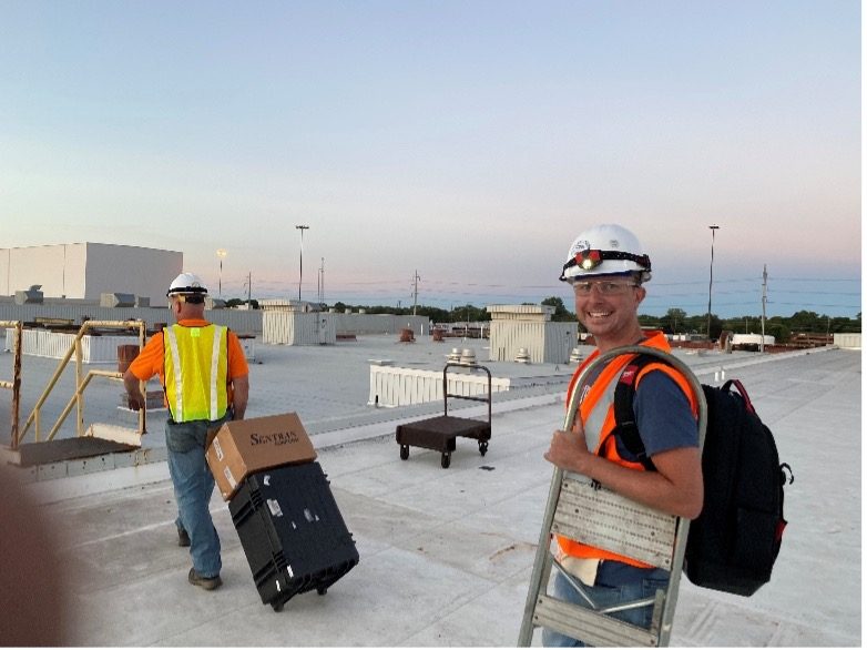 Fischer Block technicians hauling equipment across a facility rooftop at dusk