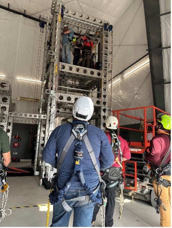 Team members in climb-safety gear at a training tower